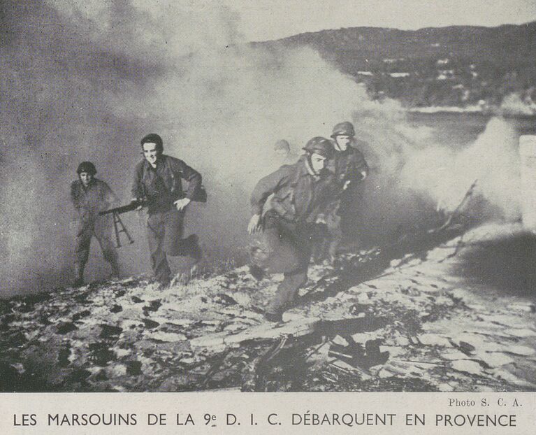Plusieurs fantassins, l'arme au poing, progressent depuis la mer qu'on aperçoit en arrière-plan